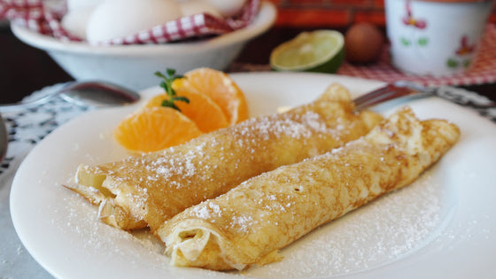 deux crêpes roulées savoureuses avec des quartiers d'oranges et du sucre glace.